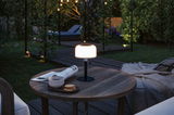Lampe de table noire moderne avec abat-jour blanc sur table en bois dans le jardin avec café et biscuits.
