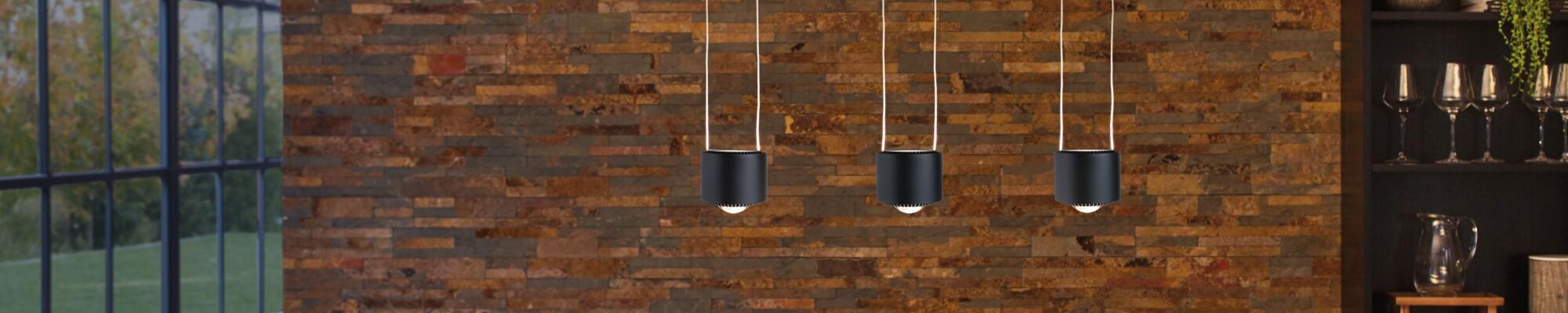 Drie zwarte metalen hanglampen tegen een rustieke bakstenen muur, moderne binnenverlichting.