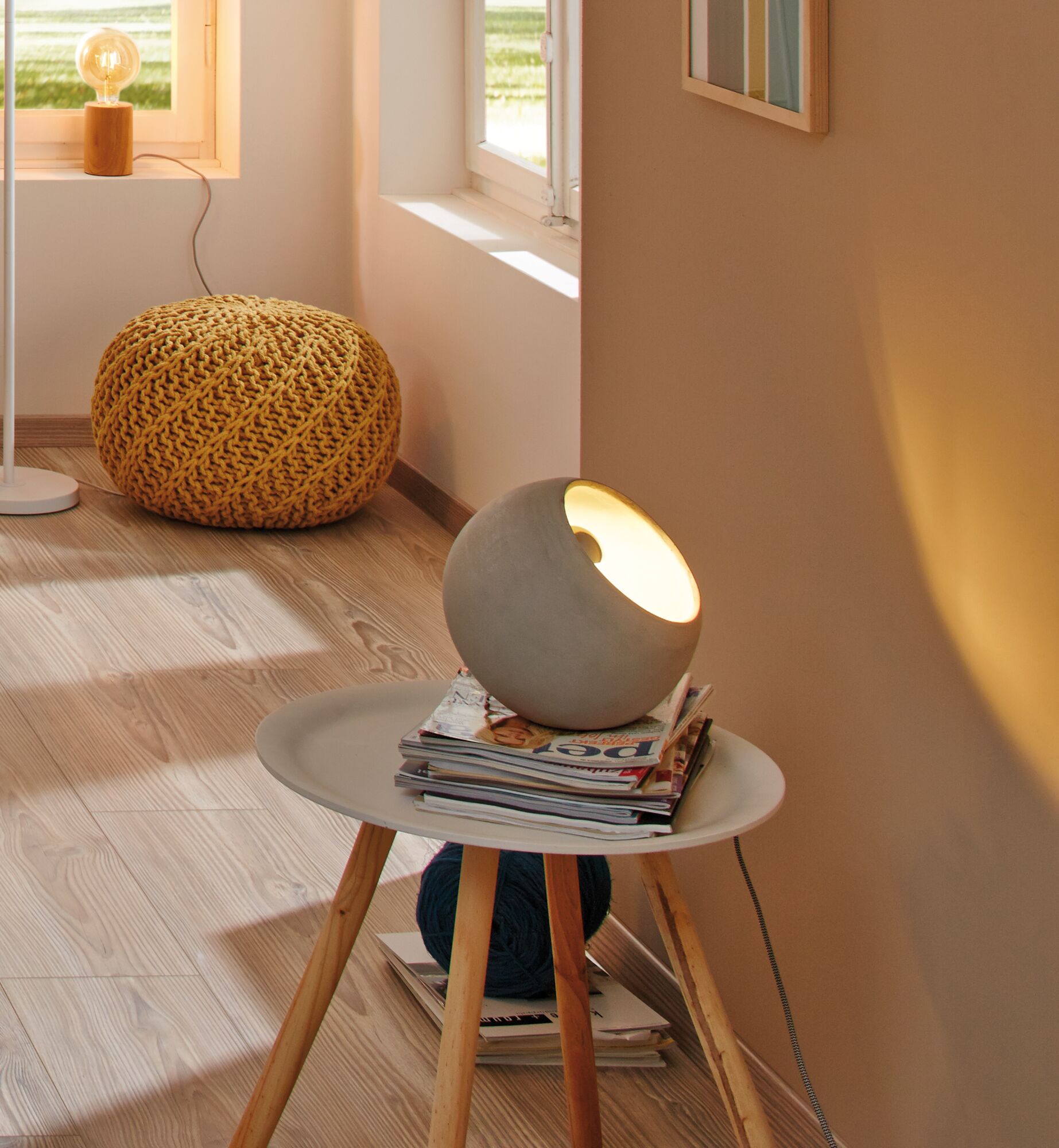 Ronde grijze betonnen tafellamp op witte bijzettafel met houten poten in moderne woonkamer.