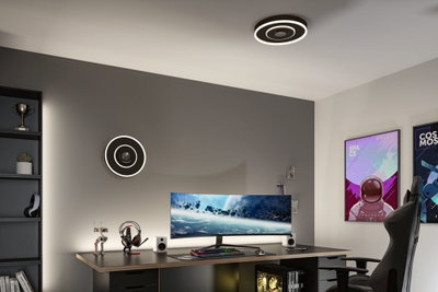 Modern office with black circular LED ceiling light emitting warm white light above gaming desk setup