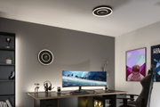 Modern office with black circular LED ceiling light emitting warm white light above gaming desk setup