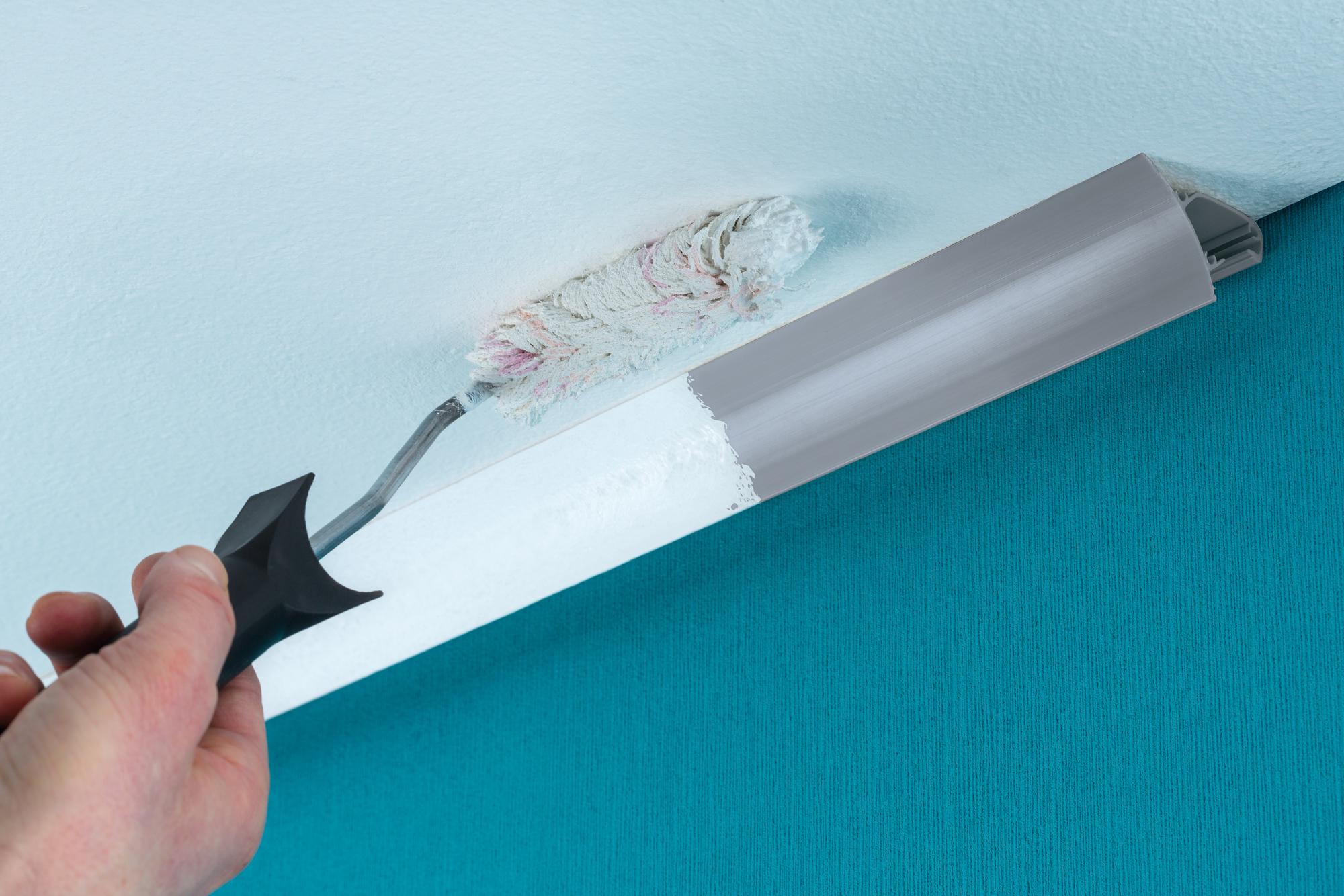 Hånd maler hvidt loft med rulle ved grå liste over turkis væg under renovering