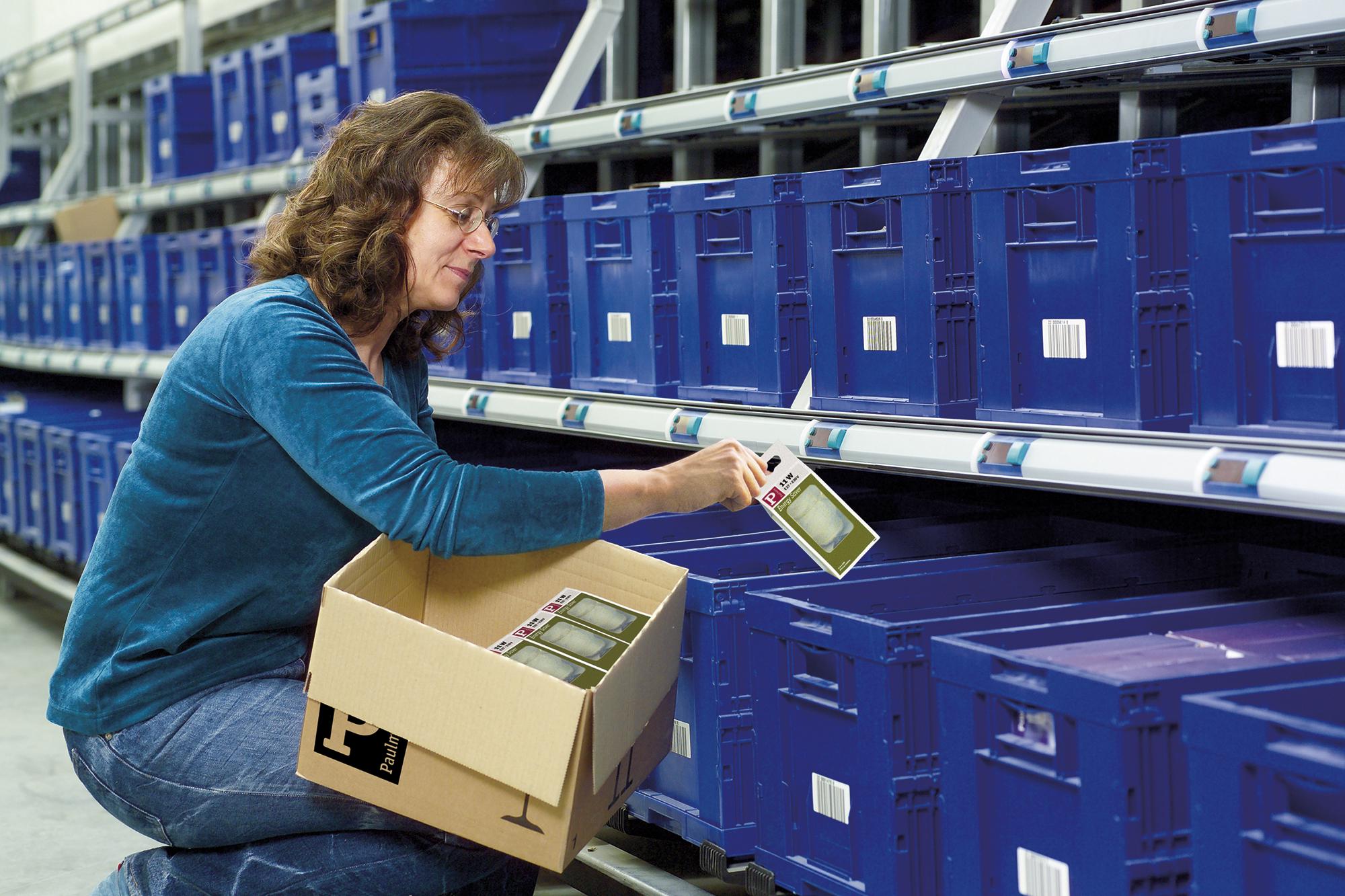 Frau kommissioniert LED-Leuchten aus Karton in blauem Lagerregal mit Barcode-Etiketten
