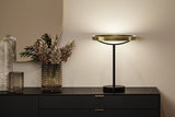 Modern table lamp with gold metal ring and black stand on black sideboard with decorative vase.