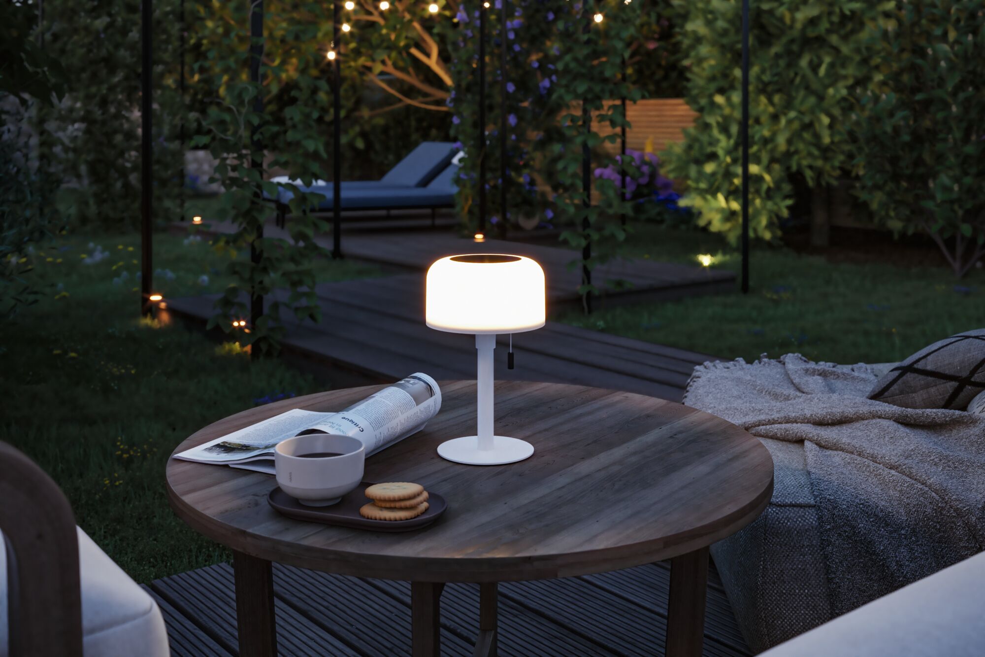 Weiße LED-Tischleuchte aus Metall auf Holztisch mit Kaffee und Keksen im Garten bei Abendlicht