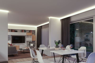 Salon moderne avec éclairage LED indirect blanc chaud au plafond, design minimaliste avec meubles blancs.