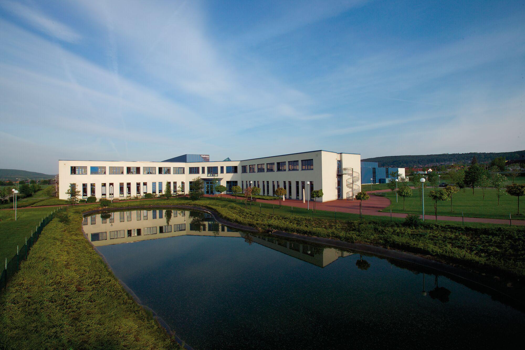 Modern office building with white facade and large windows beside pond and green lawn under blue sky