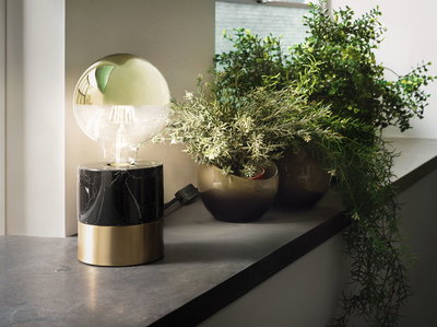 Modern table lamp with black marble and brass base beside green plants on windowsill