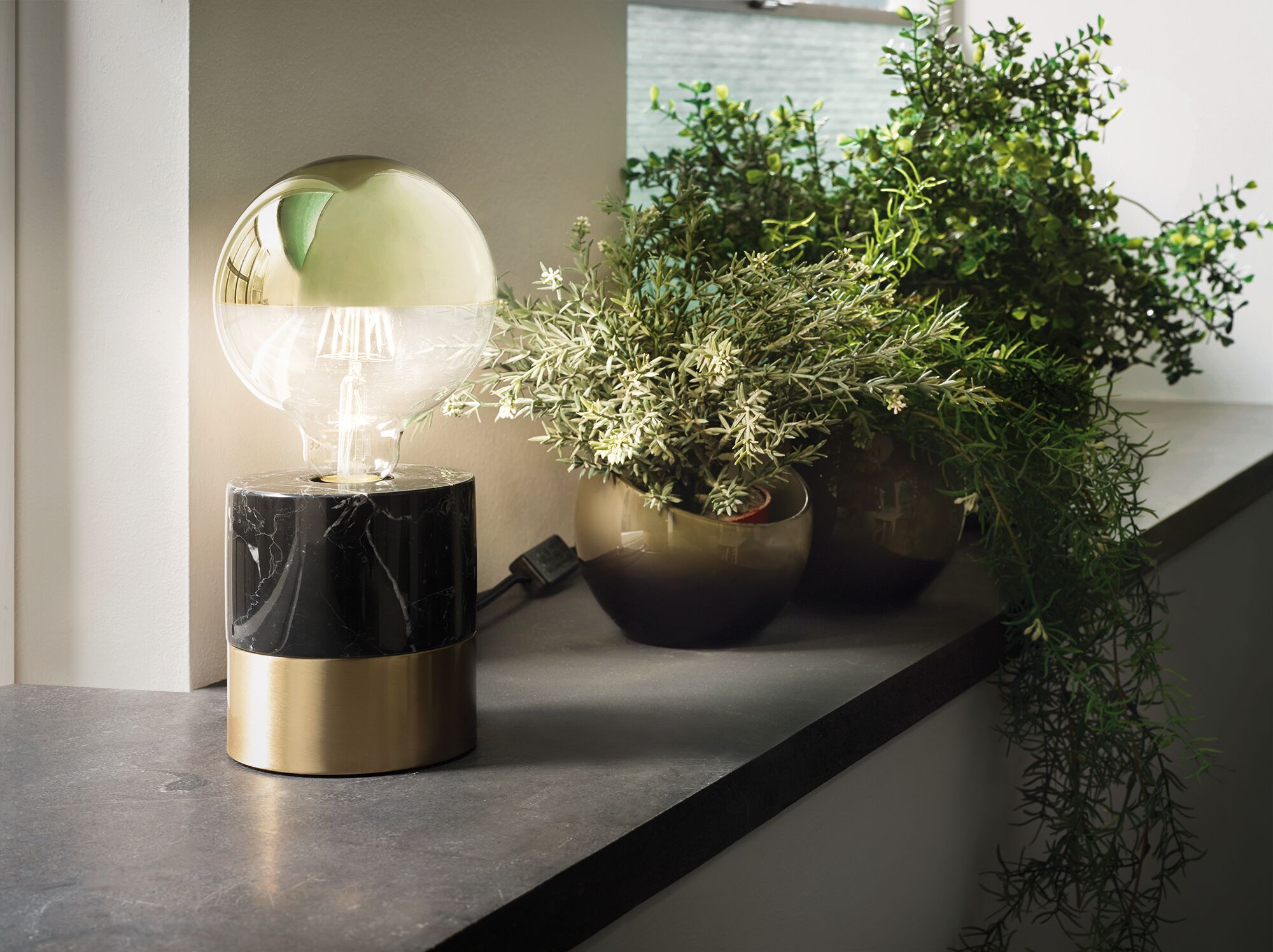 Moderne Tischlampe mit schwarzem Marmor- und Messingfuß neben grünen Pflanzen auf Fensterbank