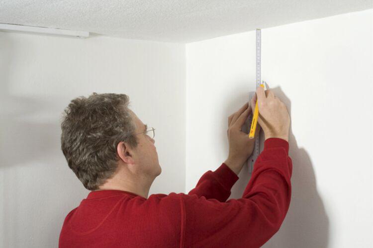 Homme en pull rouge mesurant la hauteur du mur avec une règle et un crayon pour installation d'éclairage.