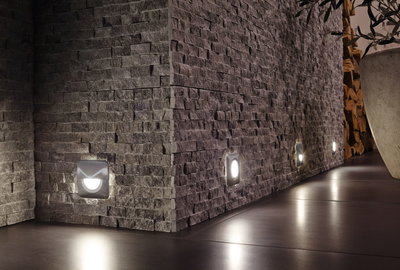 Moderne quadratische LED-Wandlichter in Edelstahl an grauer Steinwand für stimmungsvolle Bodenbeleuchtung.