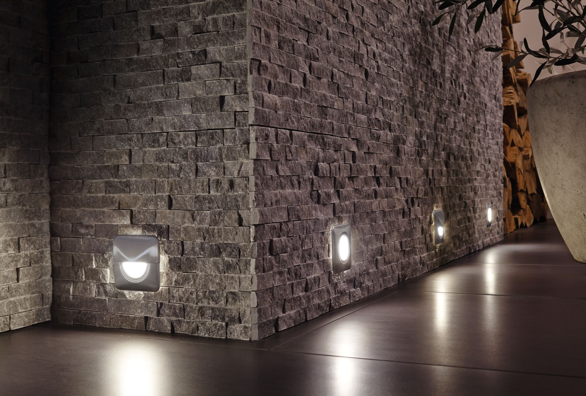 Moderne quadratische LED-Wandlichter in Edelstahl an grauer Steinwand für stimmungsvolle Bodenbeleuchtung.