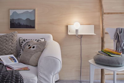 White sofa with patterned cushions beside modern wall lamp with glass globe and wooden decor.