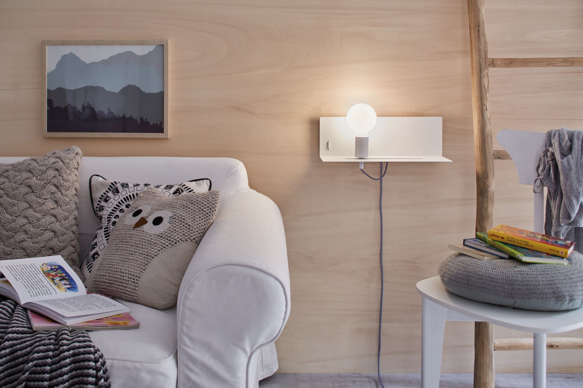 Weißes Sofa mit gemusterten Kissen neben moderner Wandlampe mit Glaskugel und Holzdekor.