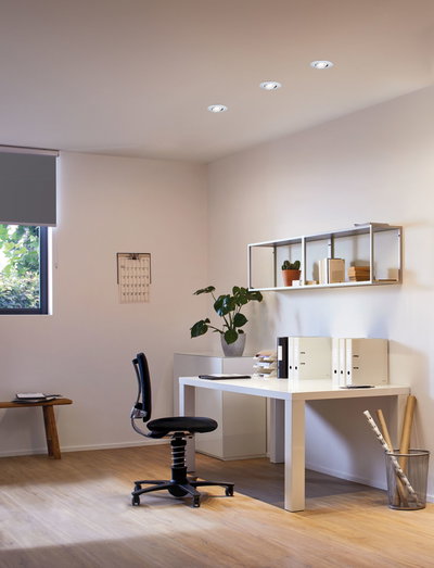 Bureau moderne avec bureau blanc, chaise de bureau noire et trois spots encastrés blancs au plafond.