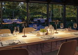 Modern wooden dining table with black table lamps in cozy dining room overlooking garden at dusk