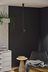 Black metal pendant light hanging from ceiling against black wall in modern living room with wooden side table.