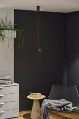 Black metal pendant light hanging from ceiling against black wall in modern living room with wooden side table.
