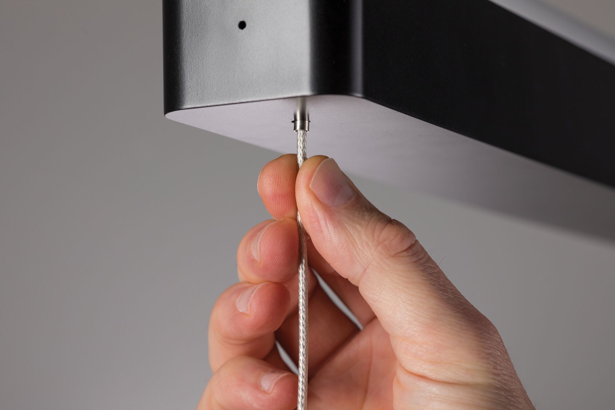 Hand holding silver steel cable attached to black metal housing of LED pendant light