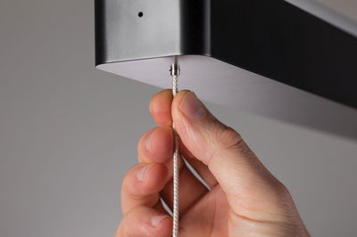 Hand holding silver steel cable attached to black metal housing of LED pendant light