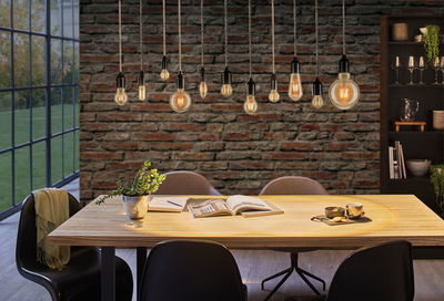 Suspensions modernes à lumière chaude au-dessus d'une table en bois dans une salle à manger avec mur en briques et chaises noires