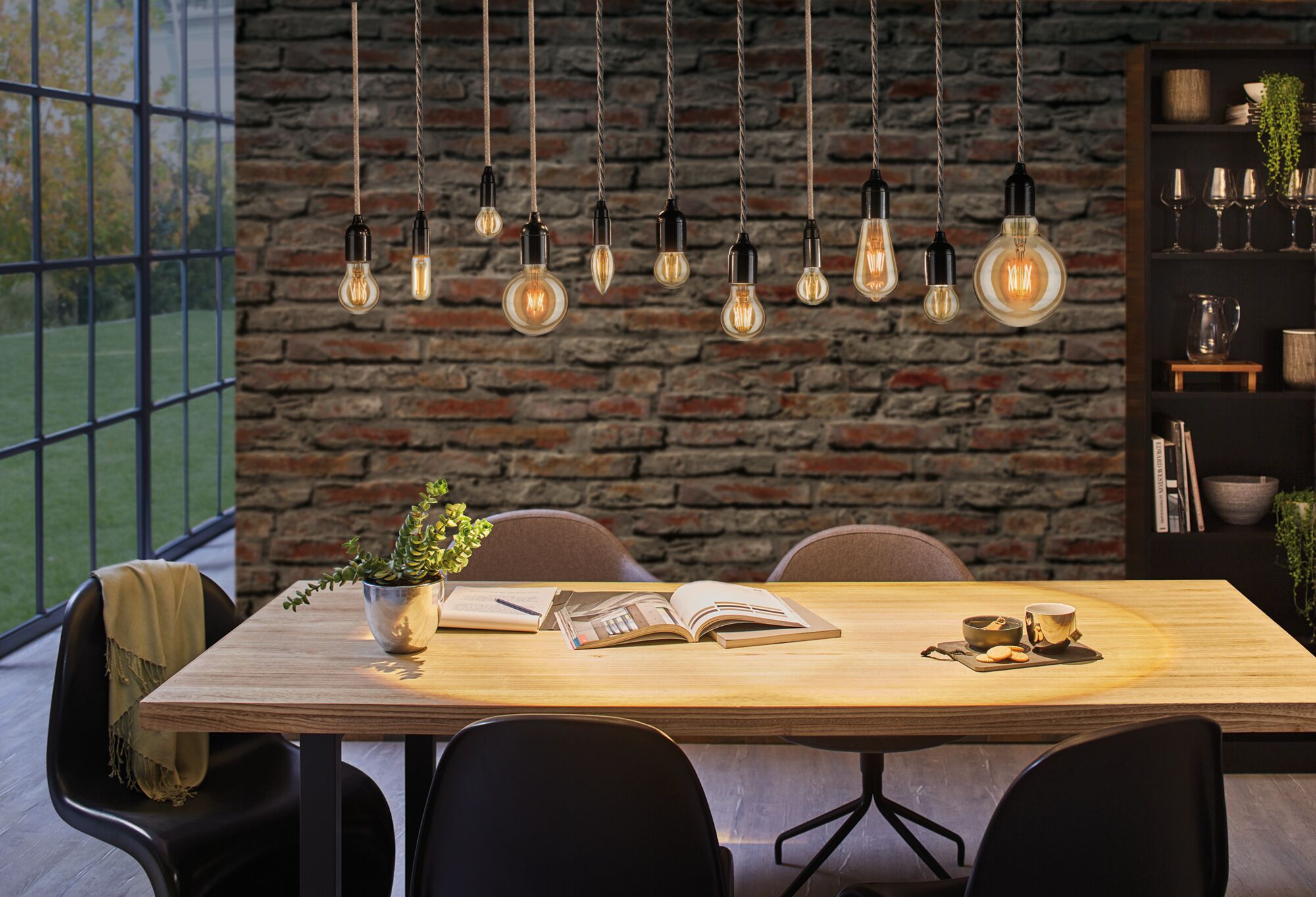 Moderne hanglampen met warm licht boven houten tafel in eetkamer met bakstenen muur en zwarte stoelen