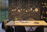 Moderne Pendelleuchten mit warmem Licht über Holztisch in Esszimmer mit Backsteinwand und schwarzen Stühlen