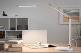 White metal LED desk lamp with adjustable arm on light wooden table with books and magazine.
