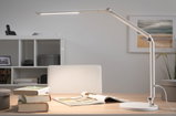 White metal LED desk lamp with adjustable arm on light wooden table with books and magazine.
