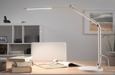White metal LED desk lamp with adjustable arm on light wooden table with books and magazine.