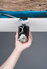 Hand hält schwarzen Einbaustrahler mit Metallrand zur Deckenmontage mit Kabel und Dämmung