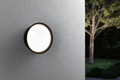 Round outdoor wall light with black frame and warm white glow on grey wall in garden