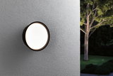 Round outdoor wall light with black frame and warm white glow on grey wall in garden