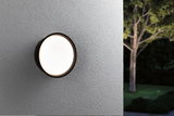 Ronde buitenwandlamp met zwart frame en warm wit licht op grijze muur in tuin