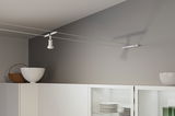 Spot câble moderne blanc en métal sur mur gris au-dessus d'un meuble de cuisine blanc avec vaisselle.