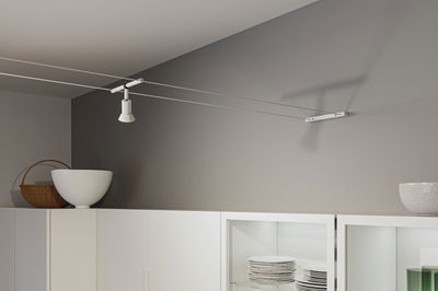 Spot câble moderne blanc en métal sur mur gris au-dessus d'un meuble de cuisine blanc avec vaisselle.
