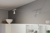 Moderner weißer Seilstrahler aus Metall an grauer Wand über weißem Küchenschrank mit Geschirr.
