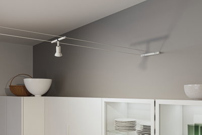 Moderner weißer Seilstrahler aus Metall an grauer Wand über weißem Küchenschrank mit Geschirr.