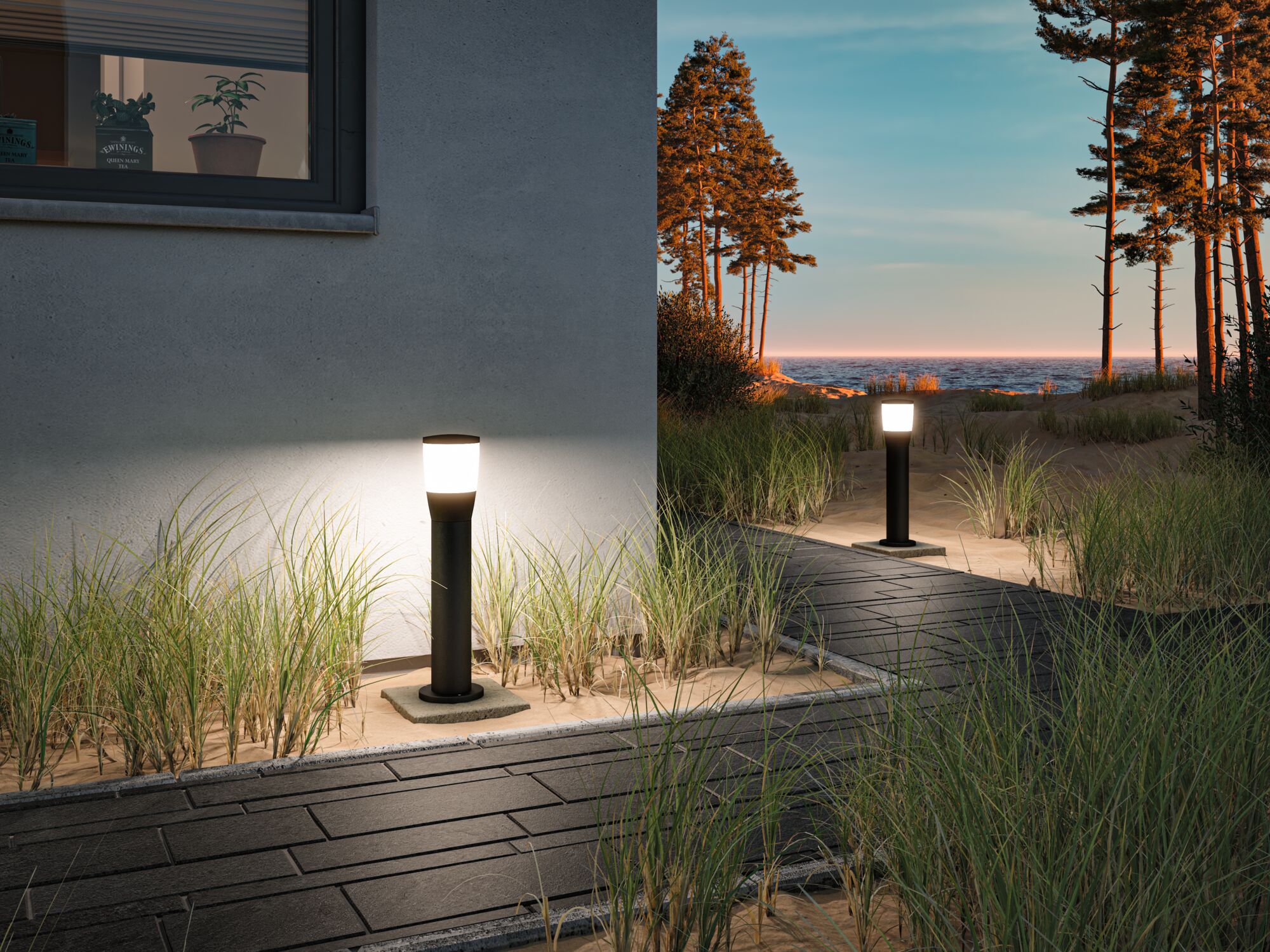 Moderne schwarze Außenleuchten mit weißem Licht entlang eines Gartenwegs am Meer bei Sonnenuntergang