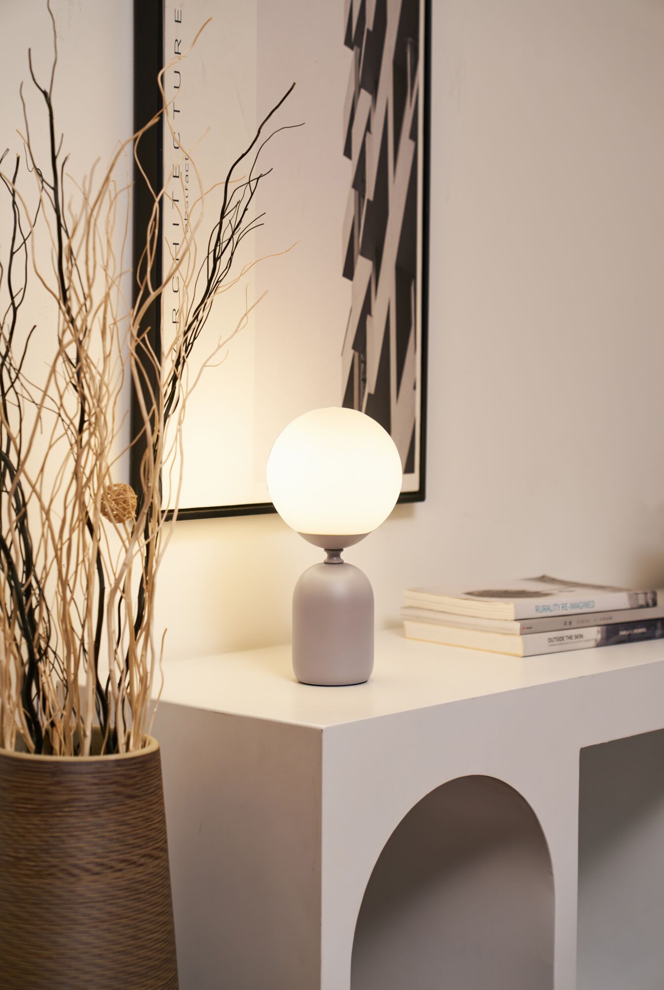 Modern table lamp with round white glass and grey metal base on white sideboard with decor.