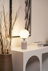 Lampe de table moderne avec globe en verre blanc et base grise sur meuble blanc avec déco.