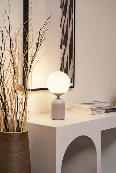 Lampe de table moderne avec globe en verre blanc et base grise sur meuble blanc avec déco.