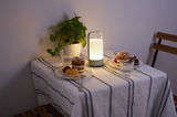 Modern portable white LED table lamp on set table with cake and plant for cozy ambient lighting