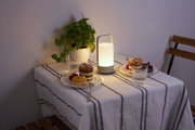 Modern portable white LED table lamp on table with cakes and green plant for cozy lighting