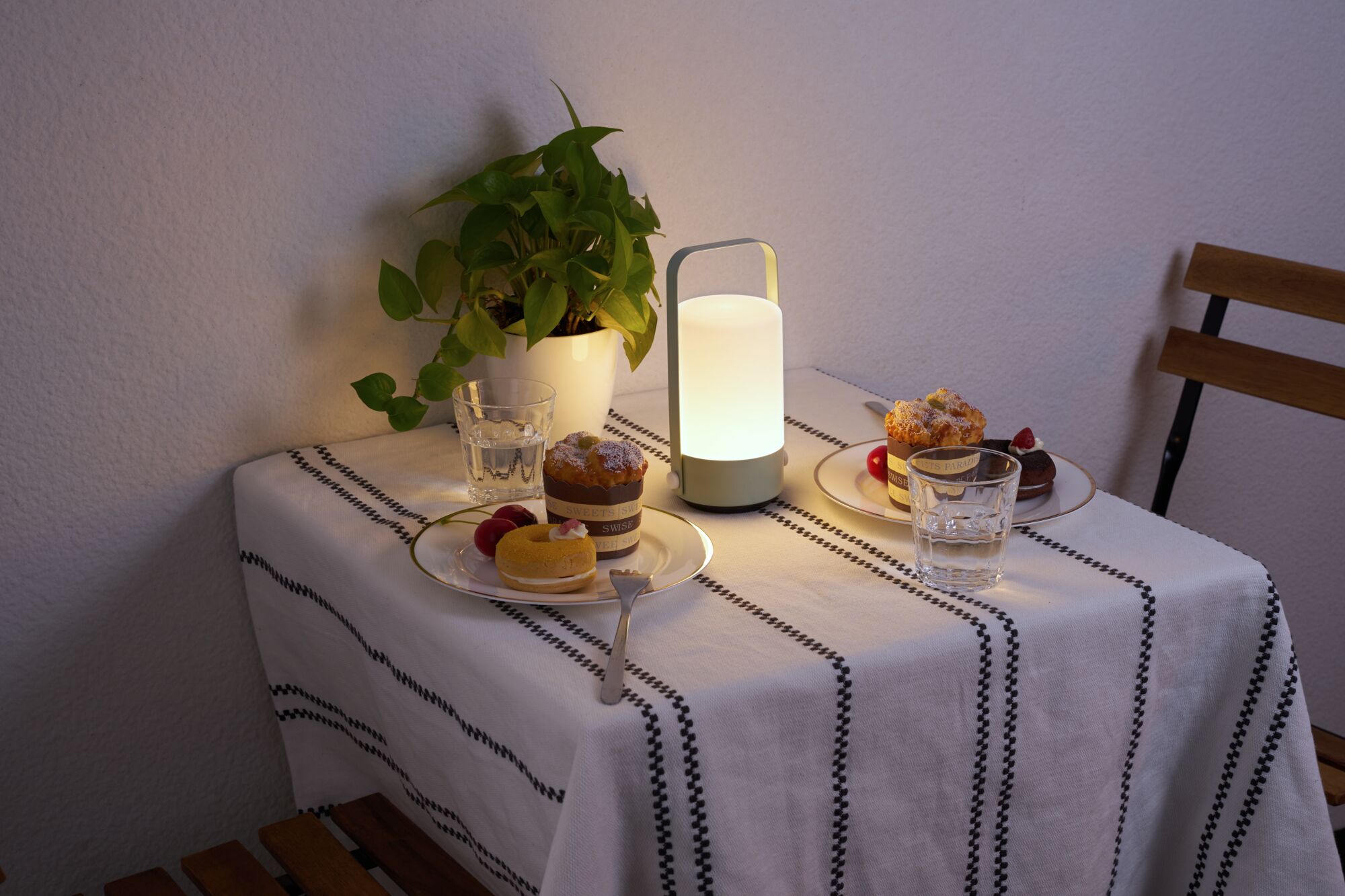 Modern portable white LED table lamp on table with cakes and green plant for cozy lighting
