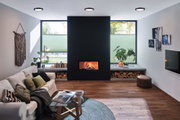 Modern living room with black fireplace, wood storage, green plants and round black ceiling lights
