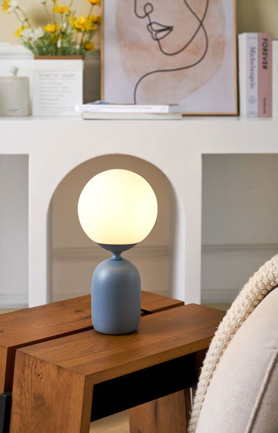 Moderne bordlampe med matblå metalfod og rund hvid glaslyskilde til stuebelysning