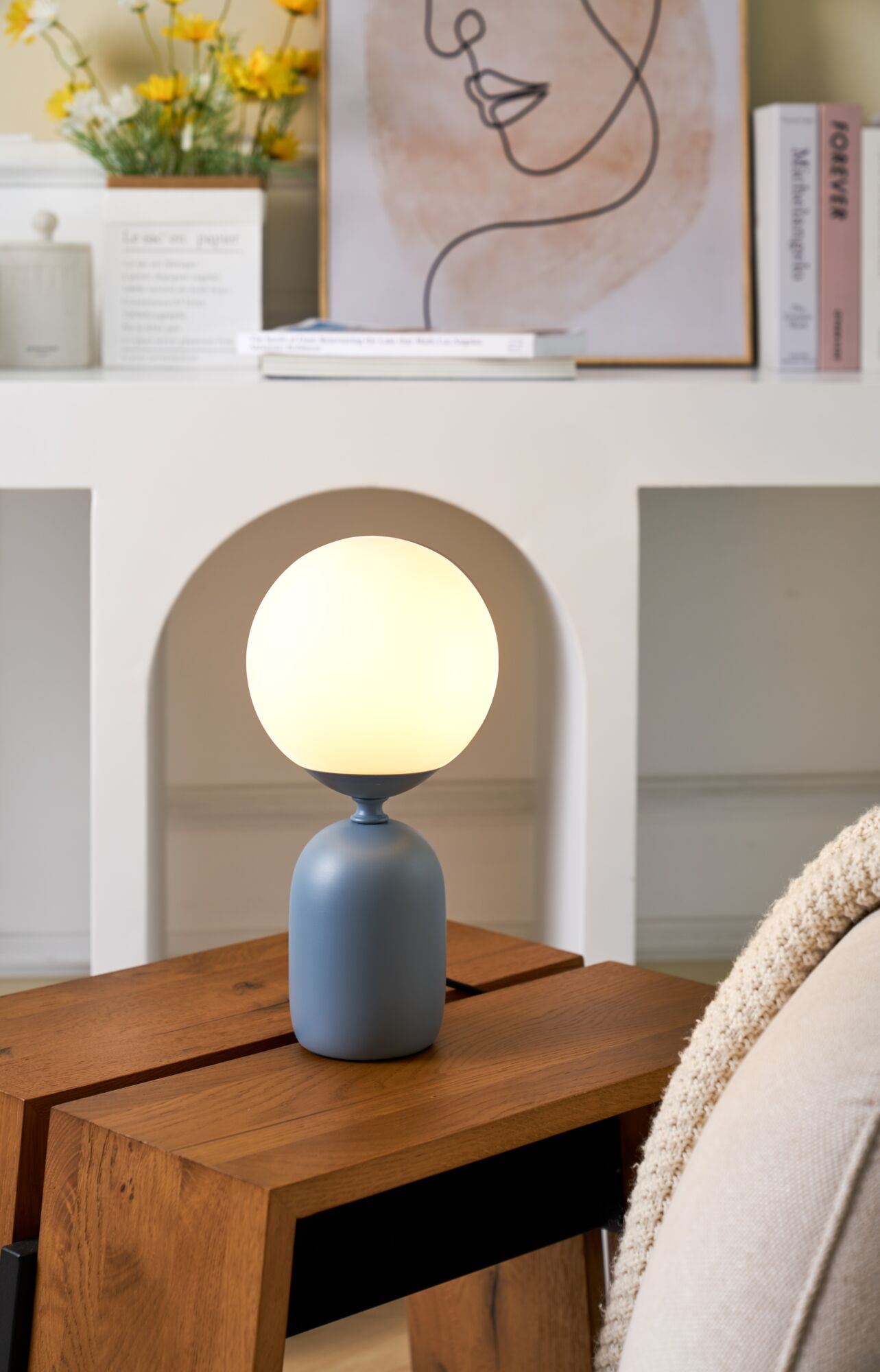 Modern table lamp with matte blue metal base and round white glass shade in cozy living room