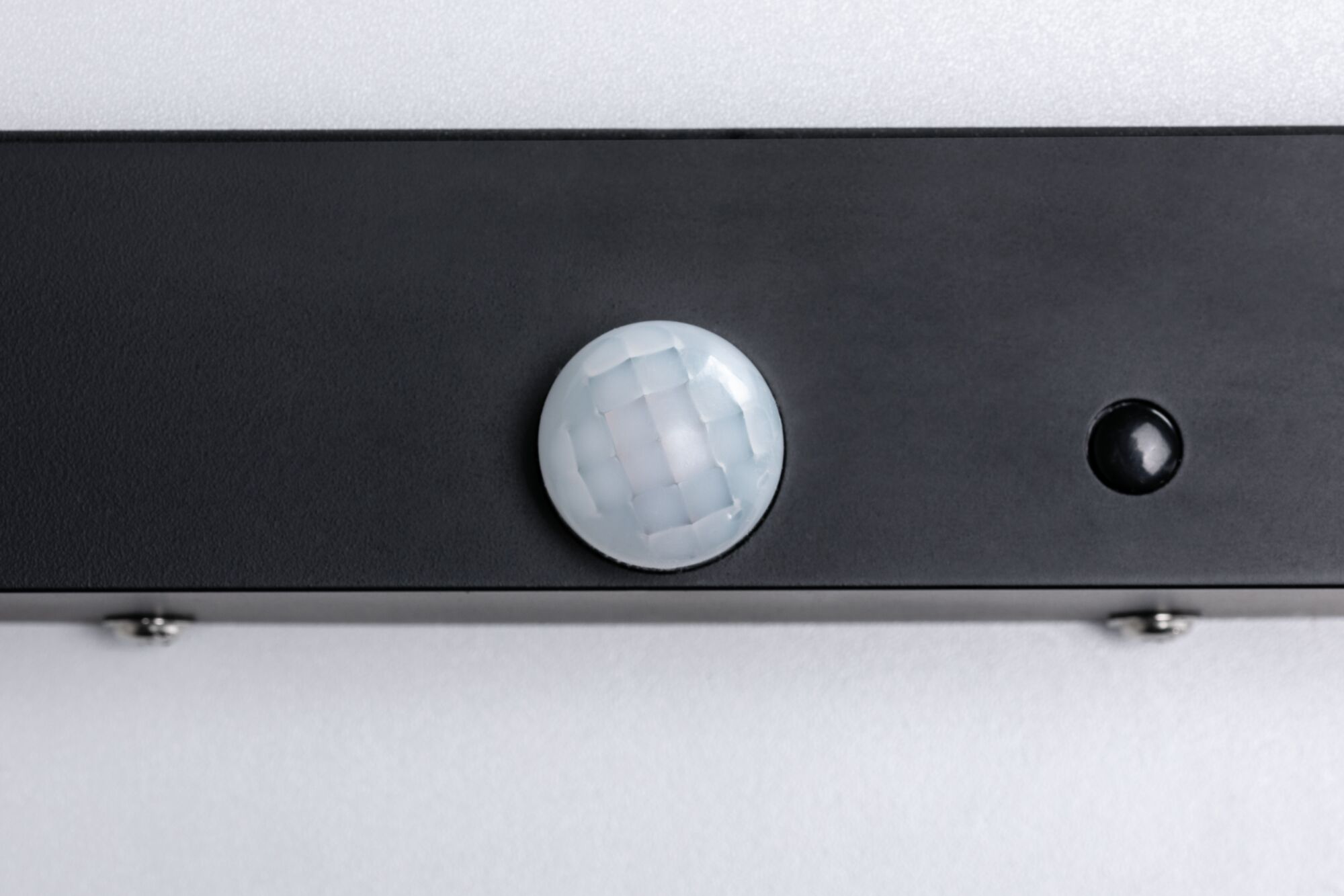 Nahaufnahme eines schwarzen Sensors mit weißer, facettierter Linse auf grauem Hintergrund für Lichtsteuerung