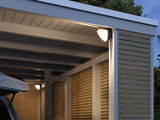 Modern outdoor wall light with white illumination on wood paneling and carport in gray and natural wood.